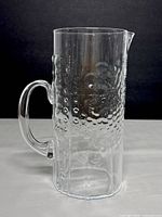 Front side view of clear glass pitcher showing textured bubbles and dot pattern with handle on left side.