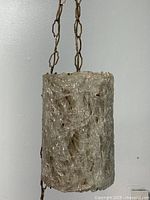 Front view of cylindrical ice-textured glass pendant lamp hanging from chain against white wall.