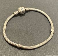 Silver Pandora bracelet coiled on a black surface, showing clasp with 'PANDORA' engraving and visible stopper rings.