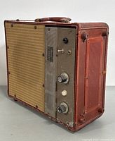 Three-quarter front view of red leather suitcase amplifier showing grille, control panel, handle and overall condition