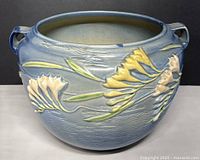 Front and side angled view of blue Roseville pottery jardiniere with floral relief design and handles