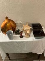 Photo of 12 miscellaneous decorative items including vase, conch shell, bowls, figurine, and jars arranged on table.