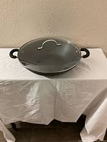 Top view of a black nonstick wok with two black handles and a glass lid with metal rim and loop handle.