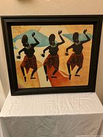 Framed silk screened painting showing three abstract human silhouettes in jewelry and red skirts with black wood frame, set against multicolored background.