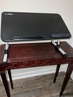 Adjustable laptop bed desk with black surface and silver aluminum legs shown on wooden table.