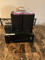 Sony receiver with speaker cables on top, two large Polk Audio speakers in background, small speaker on the left side.