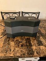 Front view of Bose Wave Music System II on a table showing front grille and attached cable.