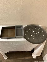 Three baking pans shown together on white tablecloth: square Calphalon pan, rectangular pan, and perforated round pizza pan.