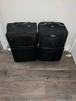 Two black carry-on rolling suitcases standing side by side on a wood floor showing overall shape and size.