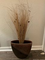 Full view of the brown ceramic vase with dried floral arrangement against a light wall