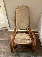Front view of the vintage rocking chair showing beige upholstered tall backrest and floral seat cushion on brown wooden frame
