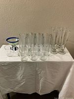 Overview of 21 assorted clear glass drinking glasses including tumblers and pilsners with one decorative glass