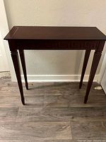 Front view of wooden console table showing carved apron and tapered legs in dark cherry finish