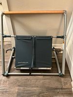 Folded ballet barre with black fabric panels displaying the Fluidity website, wooden barre, and silver metal frame on wood floor.