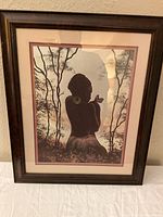 Front view of framed art print with dark brown wood frame and glass, silhouette of woman with bird and trees in background.