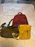 Three purses arranged on white background: red leather backpack purse, olive suede purse with studded design, and yellow leather purse with flap closure.
