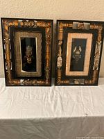 Pair of framed African tribal mask-themed artworks with detailed wooden carved frames, earth tone palette, black backgrounds, and central carved masks.