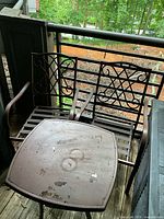 Photo of two brown metal patio chairs with decorative ornate backrests and a matching small brown metal table with visible wear.