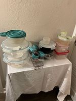 Wide view of multiple plastic food storage containers including bowls, small containers with lids, and an egg holder tray on a white tablecloth.