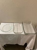 Four Pyrex glass bakeware dishes are shown side by side on a white cloth: one small round, two rectangular dishes of medium and large sizes.