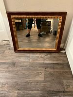 Front view of the wall mirror showing rustic wood frame with gold accents, reflective mirror surface, minor scuffs visible on frame.