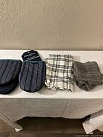 Full lots showing four kitchen towels and two oven mitts on table against wall.