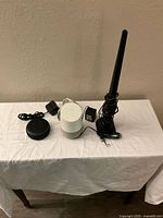Photo showing an Amazon Echo Dot, a Google Home smart speaker, and a TV antenna with their respective power adapters and cables placed on a white tablecloth.