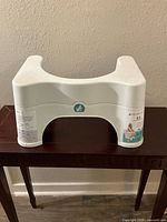 White plastic Squatty Potty 2.0 adjustable toilet stool set on a wooden table, side view showing ergonomic curved design.