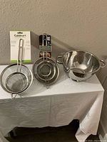 Photo showing all items together: stainless steel colander and two sets of small strainers packaged and unpackaged.
