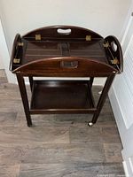 Wooden bar cart with its tray folded up showing the interior design and brass hinges.