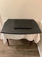 Large black wooden TV turntable resting on a table, showing flat surface with some scratches.