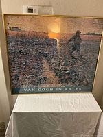 Framed exhibition poster of Vincent van Gogh painting titled 'Van Gogh in Arles' showing a figure walking in a field at sunset with visible texture of brush strokes.