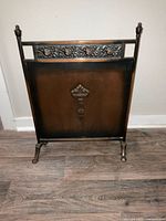 Front view of metal fireplace cover showing embossed floral decorative strip and central ornate motif, dark bronze finish.