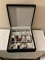 Open black watch box showing 7 watches arranged in set compartments with padded interior