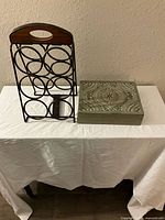 Photo of metal and wood wine rack alongside carved wooden tea box on white tablecloth.