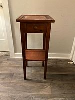 Front view of wood side table showing one drawer and lower shelf with square top and legs.