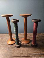 Four antique wooden thread spools on wooden surface, two empty and two with colored yarn remains.