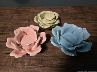 Three ceramic rose-shaped tealight holders in pink, blue, and green positioned on a wooden surface.