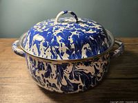 Blue and white splatter enamelware pot with lid sitting on table, showing front angle of pot and lid.