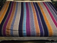 Full view of the jewel toned striped tablecloth laid out flat showing multiple vertical stripes in colors like navy, light blue, purple, orange, gold, and gray.
