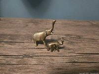 Photo of two miniature brass elephants, one larger and one smaller, on wooden surface
