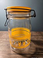Front view of the clear glass coffee jar showing yellow swing top lid with metal clasp and yellow band with COFFEE text.
