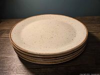 Stack of 4 speckled earth tone plates with light cream base and brown speckled pattern, displayed on wooden surface.
