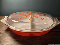 Side view of oval Pyrex divided casserole dish with clear lid, showing orange exterior and lid design.