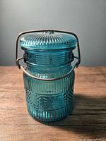 Front view of teal glass jar with metal swing top clasp, showing detailed striated and starburst glass design.