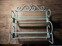 Front view of the vintage green wrought iron spice rack showing its two tiers and side scroll handles.