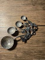 Set of four metal measuring spoons with sunflower design arranged on wooden surface
