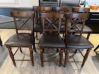 Front view of six wooden kitchen stools with dark fox leather seats aligned in a row.