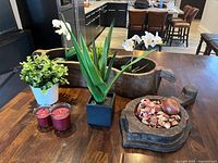 Photo showing the artificial plants, wooden flower bed centerpiece with potpourri and decorative ball, and two red candles.