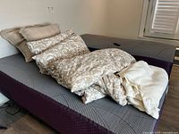 Bed setup with two beige floral patterned pillows, comforter and white mattress cover on a gray mattress base
